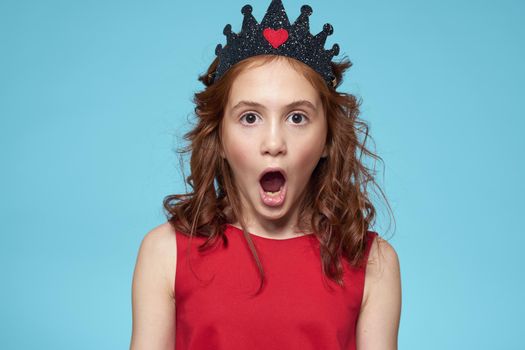 Girl with curly hair with a crown on her head red dress lifestyle blue background. High quality photo