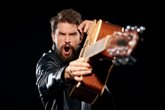A man with a guitar in his hands leather jacket music performance rock star modern style dark background. High quality photo