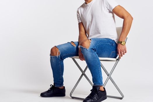 a man in jeans and a t-shirt sits on a chair on a light background side view. High quality photo