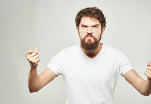 Indignant man in a white T-shirt gesturing with his hands on a light background cropped view. High quality photo