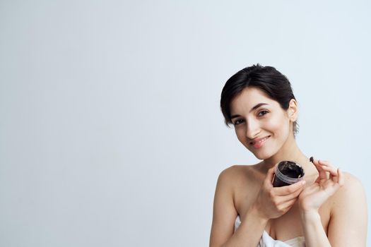 Pretty woman in white towel naked shoulders black cream in hands skin care spa procedure. High quality photo
