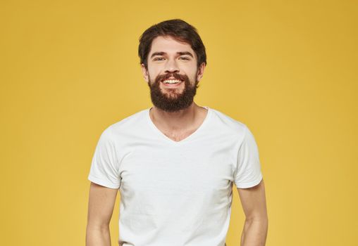 A man in a white T-shirt gestures with his hands on a yellow background Copy Space. High quality photo