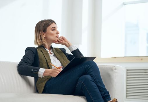 Business woman in suit with documents sitting on sofa indoors. High quality photo