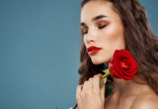 Portrait of a beautiful woman with a red flower on a blue background and evening makeup model. High quality photo