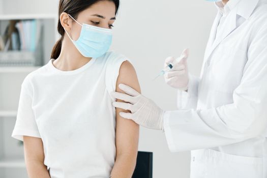 doctor in a medical gown and a mask injecting a woman in the shoulder. High quality photo