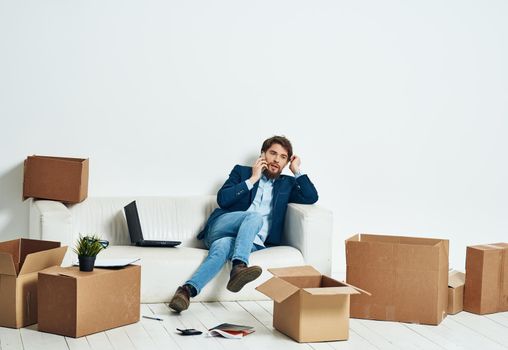 A man sits on the couch in front of a laptop working boxes with things unpacking a new office. High quality photo