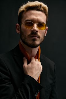 stylish man with glasses blond black jacket orange sweater dark background. High quality photo