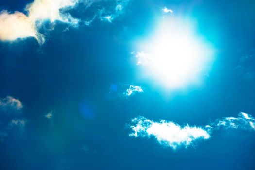 The sun in the blue sky under the clouds. Sunny day. Blue sky. Bright midday sun illuminates the space. Blue sky with clouds and sun reflection. The sun shines bright in the daytime in summer.