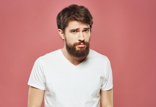 Man with a brunet beard pink background white t-shirt emotions. High quality photo