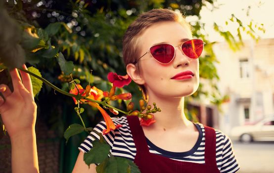 beautiful woman in glasses near red flowers on the street and red sundress striped t-shirt. High quality photo