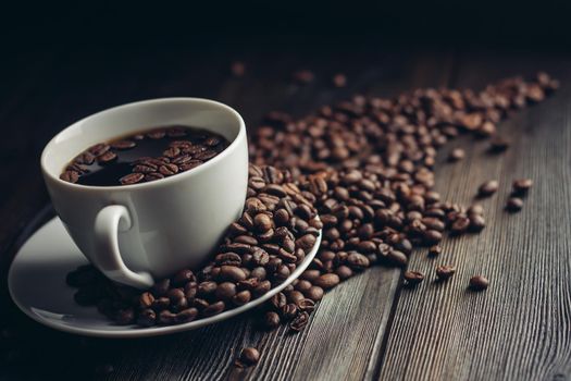 fragrant coffee beans on a wooden table and a cup with a hot drink on a saucer. High quality photo