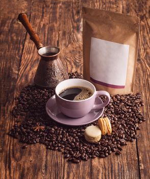 purple cup of coffee, macaroons, beans, turkish coffee pot, and craft paper pouch bag on wooden backgroun