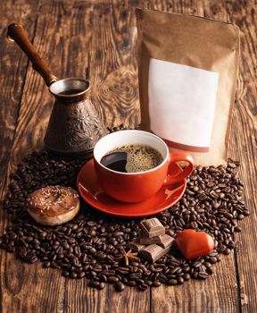 blue cup of coffee, doughnuts, heart, beans, turkish coffee pot, and craft paper pouch bag on wooden backgroun