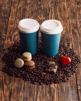 two paper cups of coffee, macaroons, beans, heart on wooden backgroun