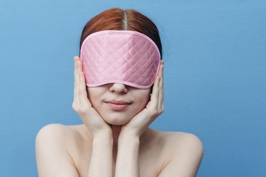 happy woman with pink sleep mask on her face on blue background. High quality photo
