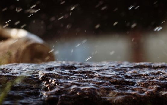 Wet stone in the rain. Rain water drop falling to the stone. Water is flowing and splashing around them.