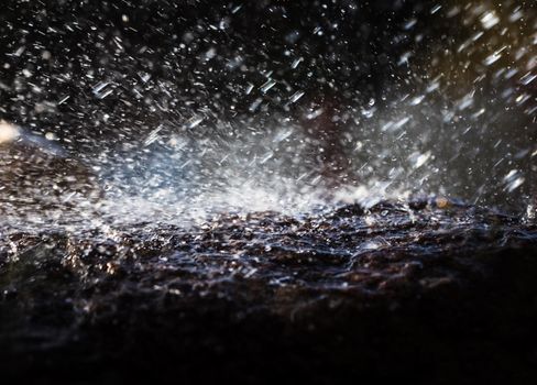 Wet stone in the rain. Rain water drop falling to the stone. Water is flowing and splashing around them.