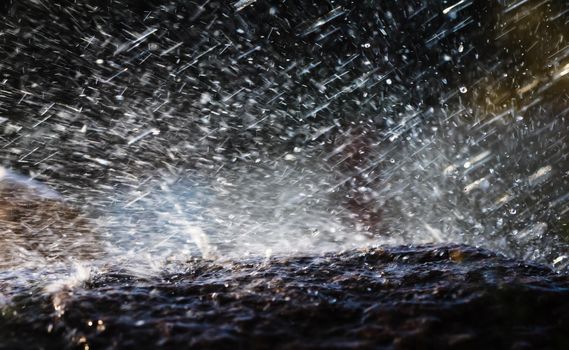 Wet stone in the rain. Rain water drop falling to the stone. Water is flowing and splashing around them.