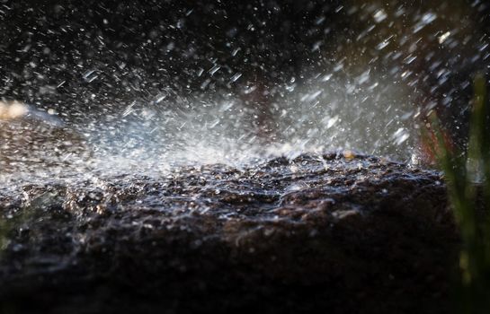 Wet stone in the rain. Rain water drop falling to the stone. Water is flowing and splashing around them.