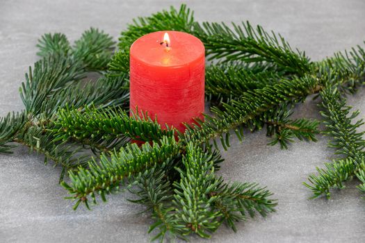Christmas motif, texture, wallpaper, background with branches of a Nordmann fir and burning red candle on a grey marbled  background 