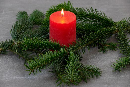 Christmas motif, texture, wallpaper, background with branches of a Nordmann fir and burning red candle on a grey marbled  background 