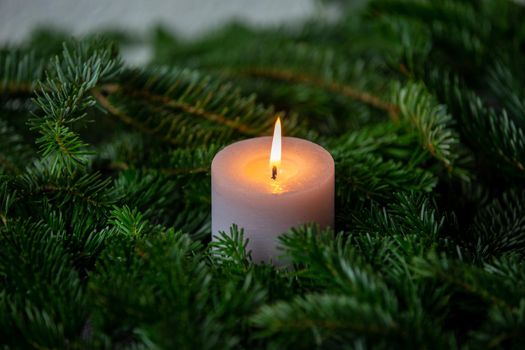 Christmas motif, texture, wallpaper, background with branches of a Nordmann fir and burning white candle on a grey marbled  background 