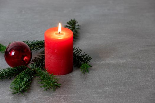 Christmas motif with red burning candle,  Nordmann fir branches and red christmas tree balls on a dark grey marbled  background with free space for text
