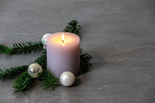 Christmas motif with white burning candle,  Nordmann fir branches and silver colored christmas tree balls on a dark grey marbled  background with free space for text
