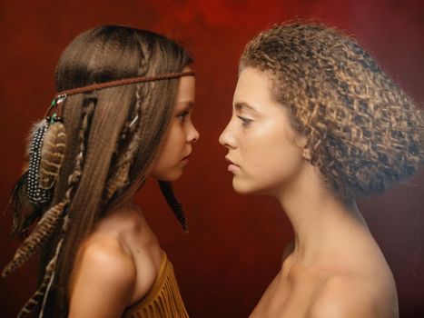 Beautiful girl with a feather in her hair and woman aborigines red background family Indian tribe. High quality photo