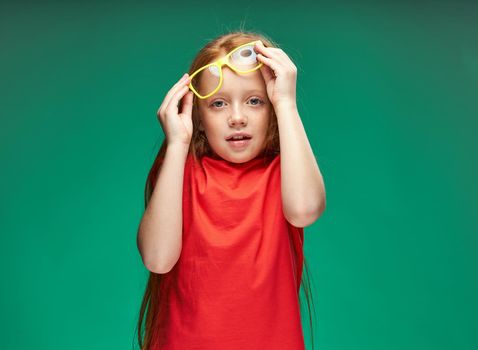 cheerful red-haired girl holding glasses in her hands learning school green background. High quality photo