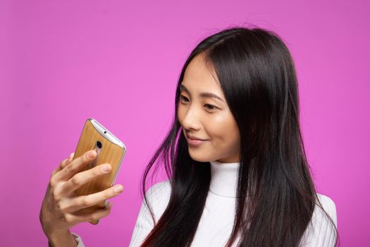 cheerful pretty brunette with a phone in her hands communication internet technology pink background. High quality photo