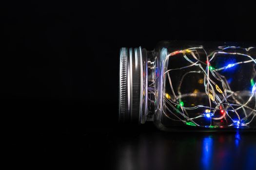 Colorful fairy lights in glass jar isolated on black background.