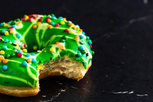 Green glazed donut with sprinkles isolated. Close up of colorful bitten donut.