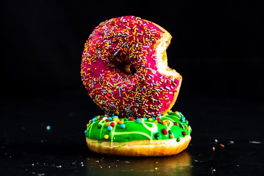 Bitten pink glazed donut with sprinkles isolated. Close up of colorful donuts.