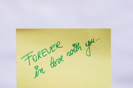 Forever in love with you handwriting text close up isolated on yellow paper with copy space.