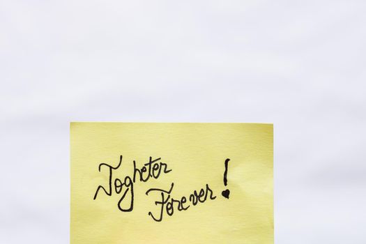 Togheter forever handwriting text close up isolated on yellow paper with copy space.