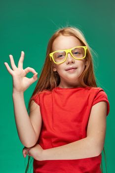 redhead girl with yellow glasses gesturing with her hands childhood learning Green background. High quality photo