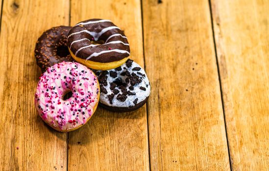 Colorful donuts on wooden table. Sweet icing sugar food with glazed sprinkles, doughnut with chocolate frosting. Top view with copy space