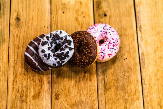 Colorful donuts on wooden table. Sweet icing sugar food with glazed sprinkles, doughnut with chocolate frosting. Top view with copy space