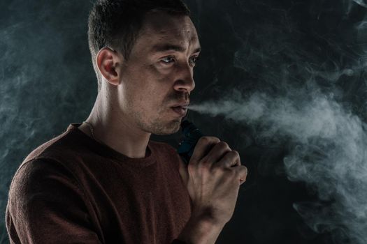 a man smokes a vape on a black background white smoke steam portrait close-up. High quality photo