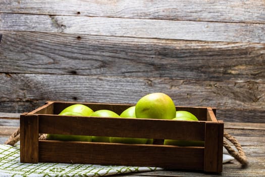 Wooden crate with ripe green apples on wooden table.