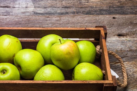 Wooden crate with ripe green apples on wooden table.