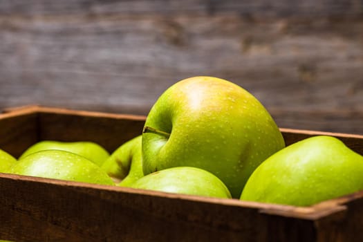 Wooden crate with ripe green apples on wooden table.