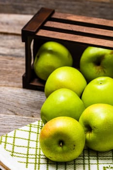 Wooden crate with ripe green apples on wooden table.