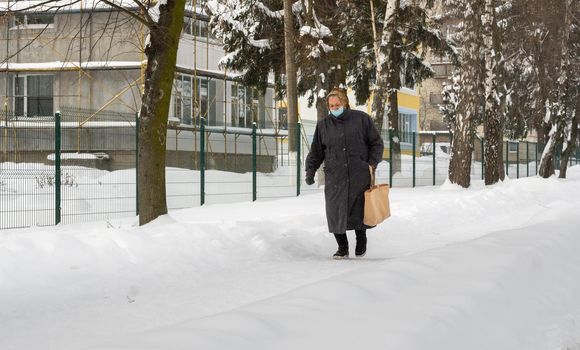 Lutsk, Ukraine - February 12,2020: City street after blizzard. Record-breaking amounts of snow. Health protection. Woman wearing face mask on public street in middle of coronavirus epidemic in winter