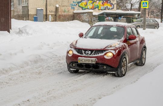 Lutsk, Ukraine - February 12,2020: Stuck car in snow and ice. City street after blizzard. Buried vehicle in snowdrift. Parking in winter after snowfall. Uncleaned road. Record-breaking amounts of snow