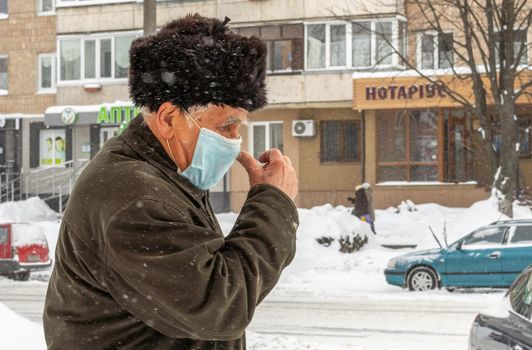 Lutsk, Ukraine - February 12,2020: Man wearing face mask on public streets in middle of coronavirus epidemic in winter. Health protection, virus outbreak prevention during infectious diseases in city