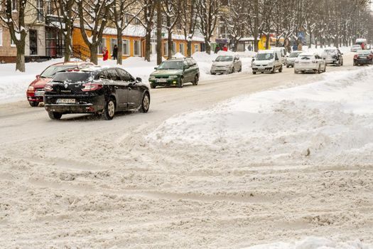 Lutsk, Ukraine - February 12,2020: Uncleaned slippery roads and sidewalk in winter. Cars in snowdrift. People on street after snow storm. City street after blizzard. Record-breaking amounts of snow