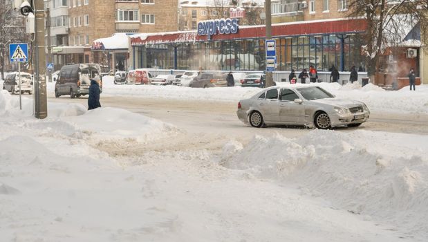 Lutsk, Ukraine - February 12,2020: People on street after snow storm. City street after blizzard. Record-breaking amounts of snow. Uncleaned slippery roads and sidewalk in winter. Cars in snowdrift