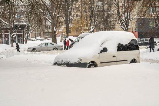 Lutsk, Ukraine - February 12,2020: Stuck car in snow and ice. City street after blizzard. Buried vehicle in snowdrift. Parking in winter after snowfall. Uncleaned road. Record-breaking amounts of snow